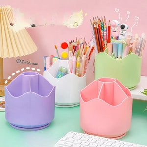 A collection of rotating pen holders and storage boxes in different colors (purple, green, white, and pink) placed on a desk with a lamp and various stationery items in the background.
