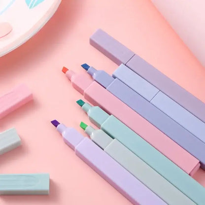 Set of pastel-colored markers and erasers on a pink background