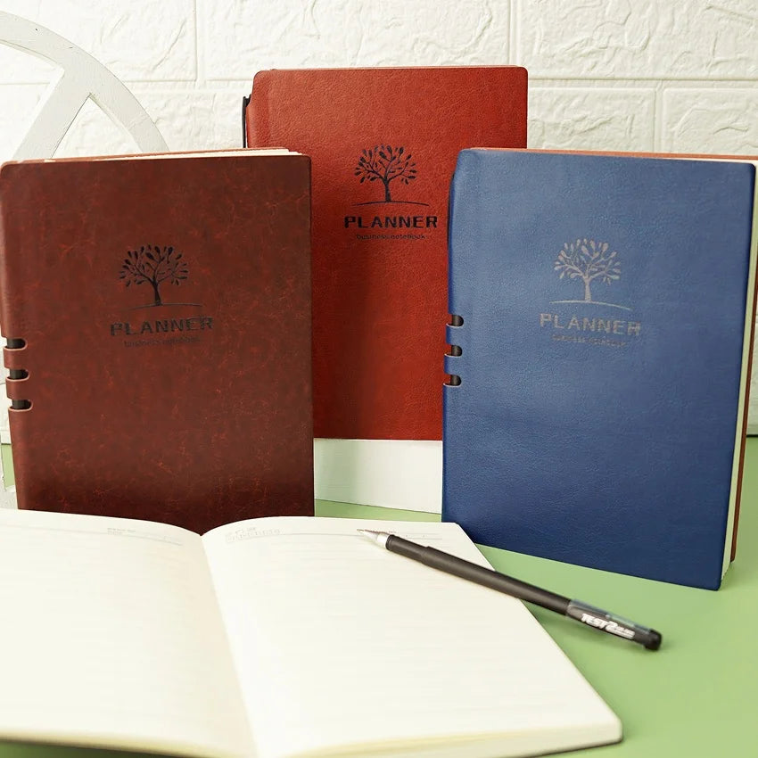 A red, blue, and black leather planner with embossed text 'PLANNER' on the cover, displayed alongside a gel pen and an open planner page.