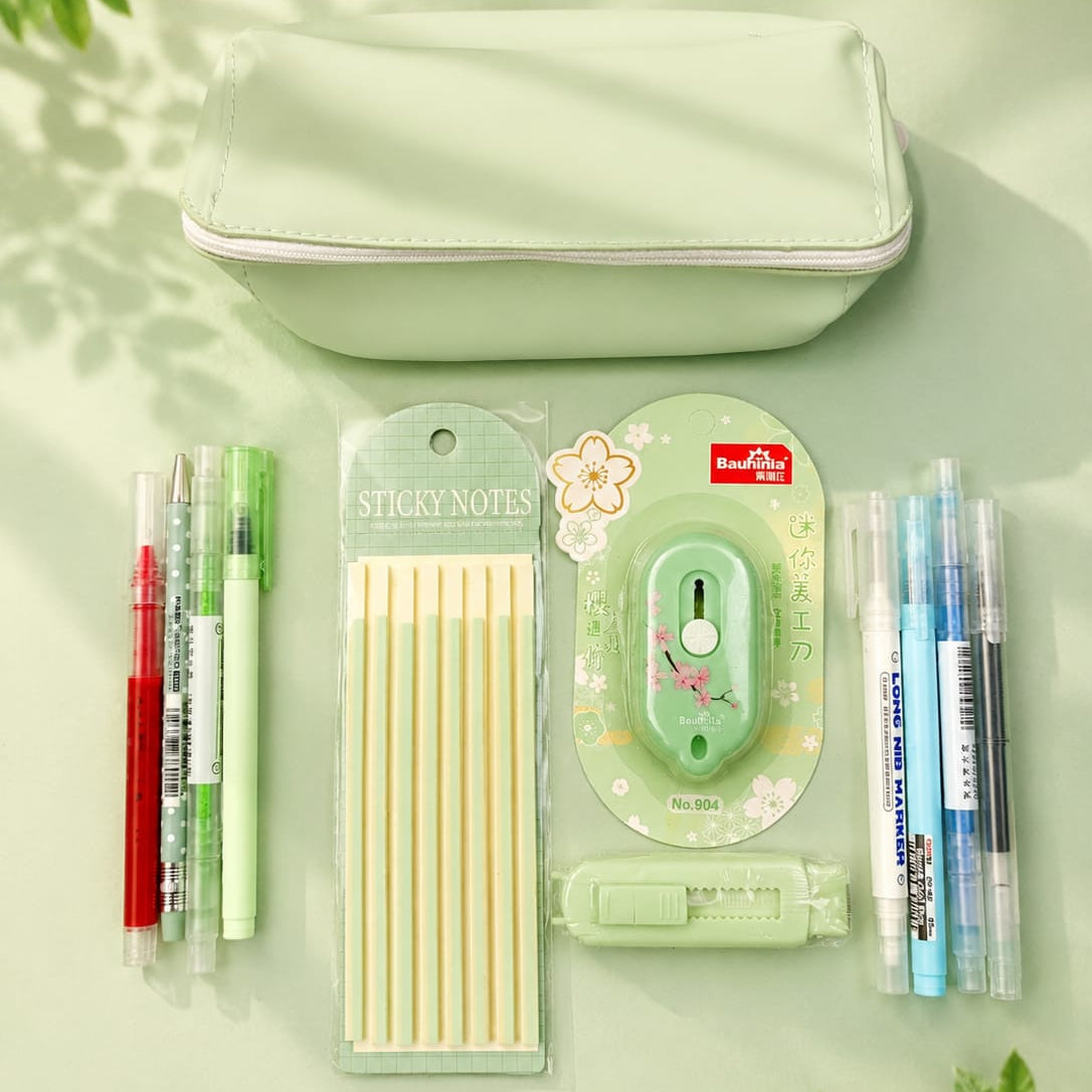 Stationery items including pens, sticky notes, and a small cutter on a light green background with leaves.