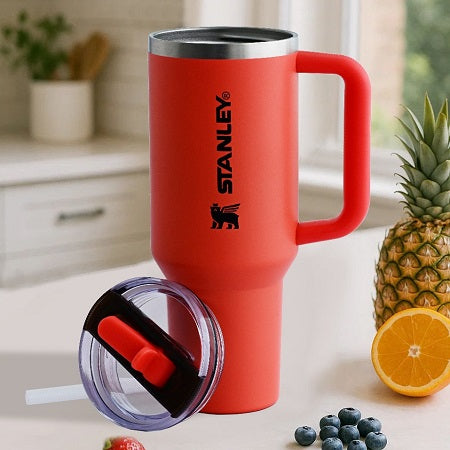 Red Stanley mug with a lid on a table with fruits