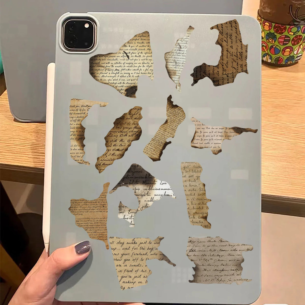 Gray tablet case with cut-out designs resembling old paper and text on a wooden surface.