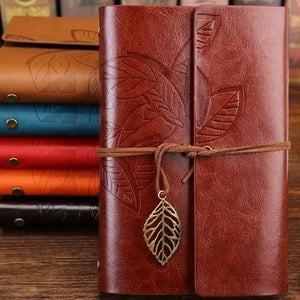 A brown leather cover journal with embossed leaf patterns, secured with a leather rope and metal leaf badge.