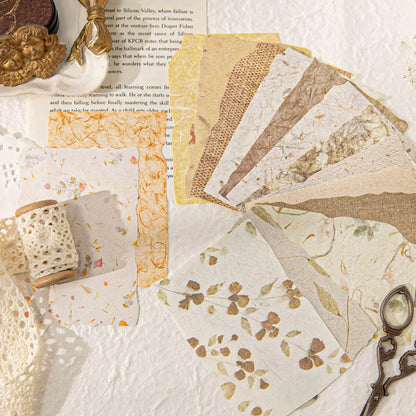 Collection of vintage-style papers with lace, a spool of thread, and an antique key on a textured surface.
