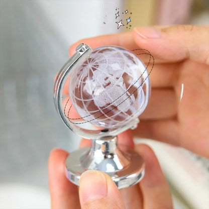 Hand holding a small glass globe with a metal stand against a blurred background