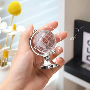 Hand holding a small globe with a blurred indoor background