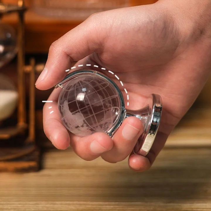 Hand holding a small crystal ball with a metallic frame on a wooden surface