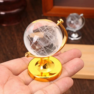 Small globe with gold base held in a hand against a blurred background