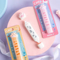 Packaged correction tapes with cat-themed designs, including a tape with paw prints and a cat face, and another with a striped cat design. Both are on a pastel background with a decorative border.