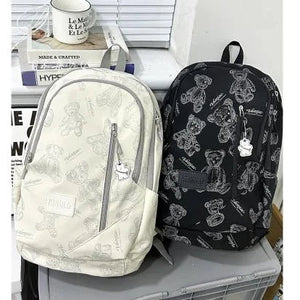 Two backpacks, one white and one black with bear patterns, on a surface.