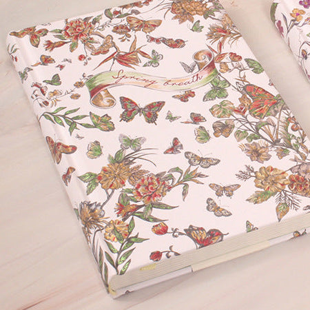 Two floral-patterned notebooks on a light wooden surface