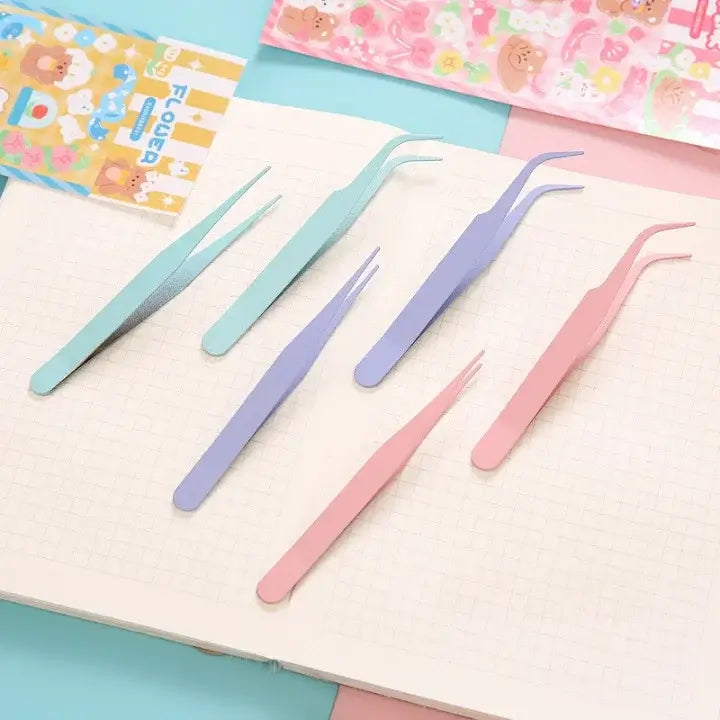Set of colorful tweezers on a light pink surface with floral-patterned paper in the background.