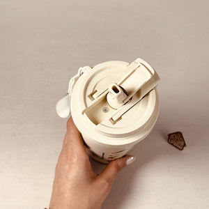 Hand holding a white ceramic mug with a lid on a beige background