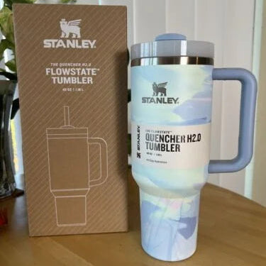 Stanley tumbler with handle next to its packaging on a wooden surface.