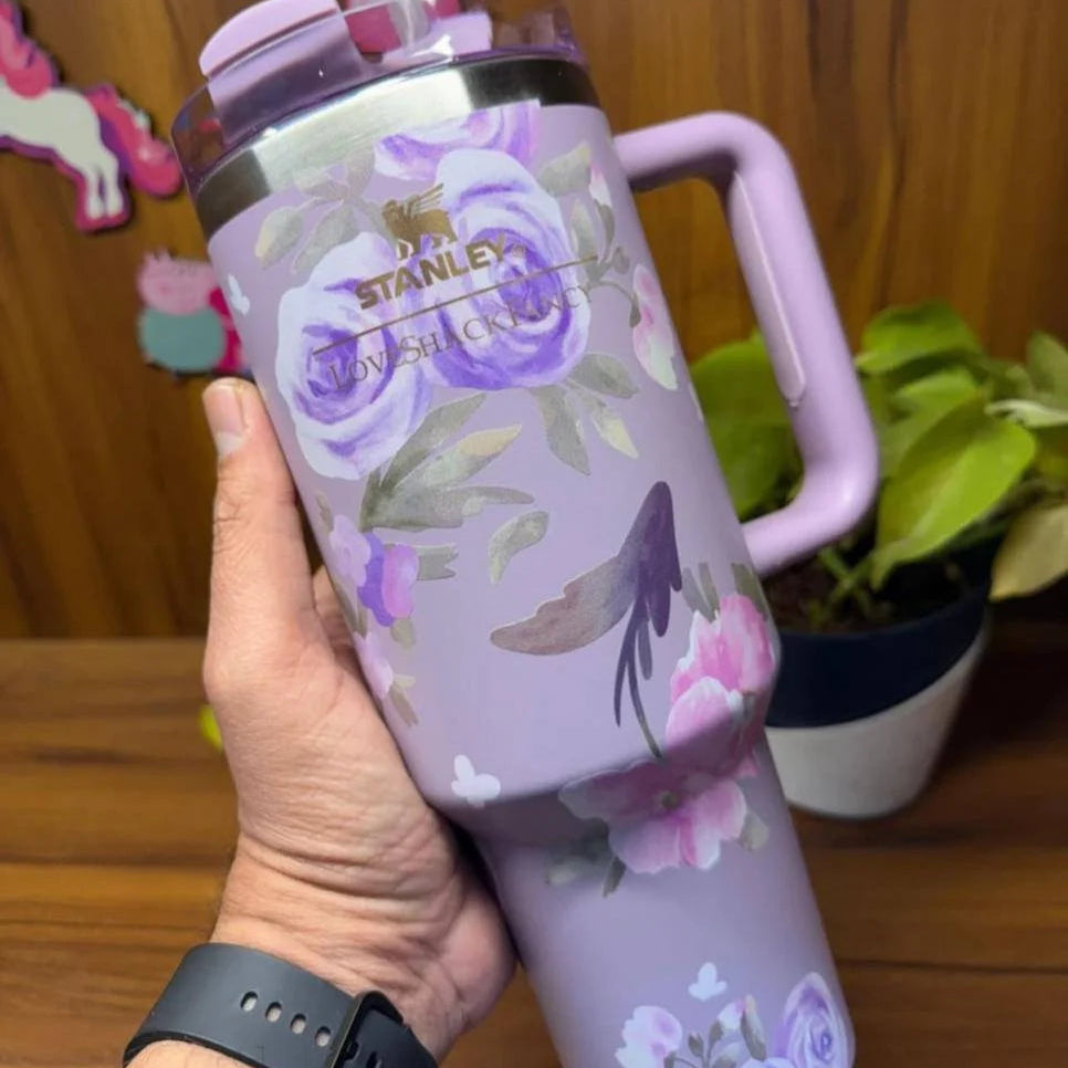 Purple floral Stanley tumbler held by a hand with a wooden background
