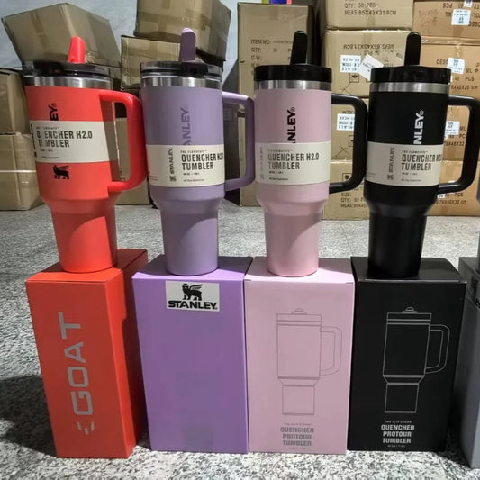 Colorful insulated mugs with 'Stanley' branding on a gray surface with cardboard boxes in the background.
