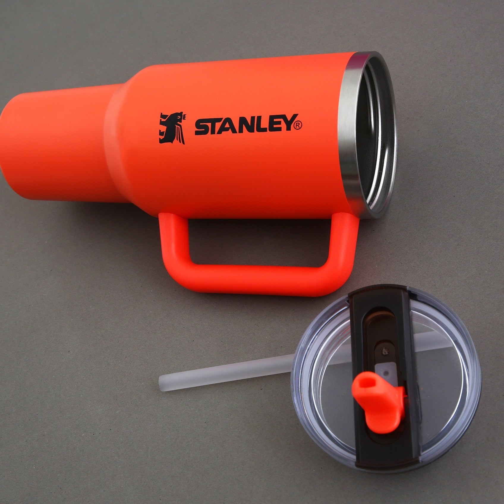 Orange Stanley tumbler with handle and straw on a gray background