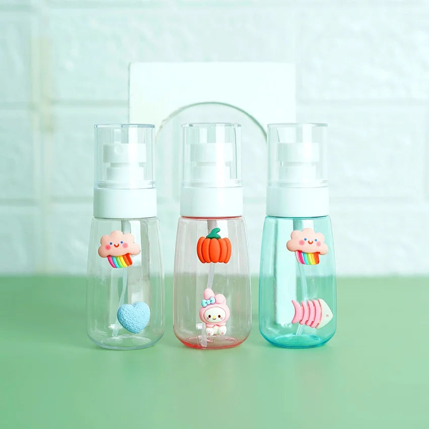Three transparent mini pocket spray bottles with 3D cartoon stickers, displayed on a green surface. From left to right, the bottles have different colored liquid levels and are refillable.