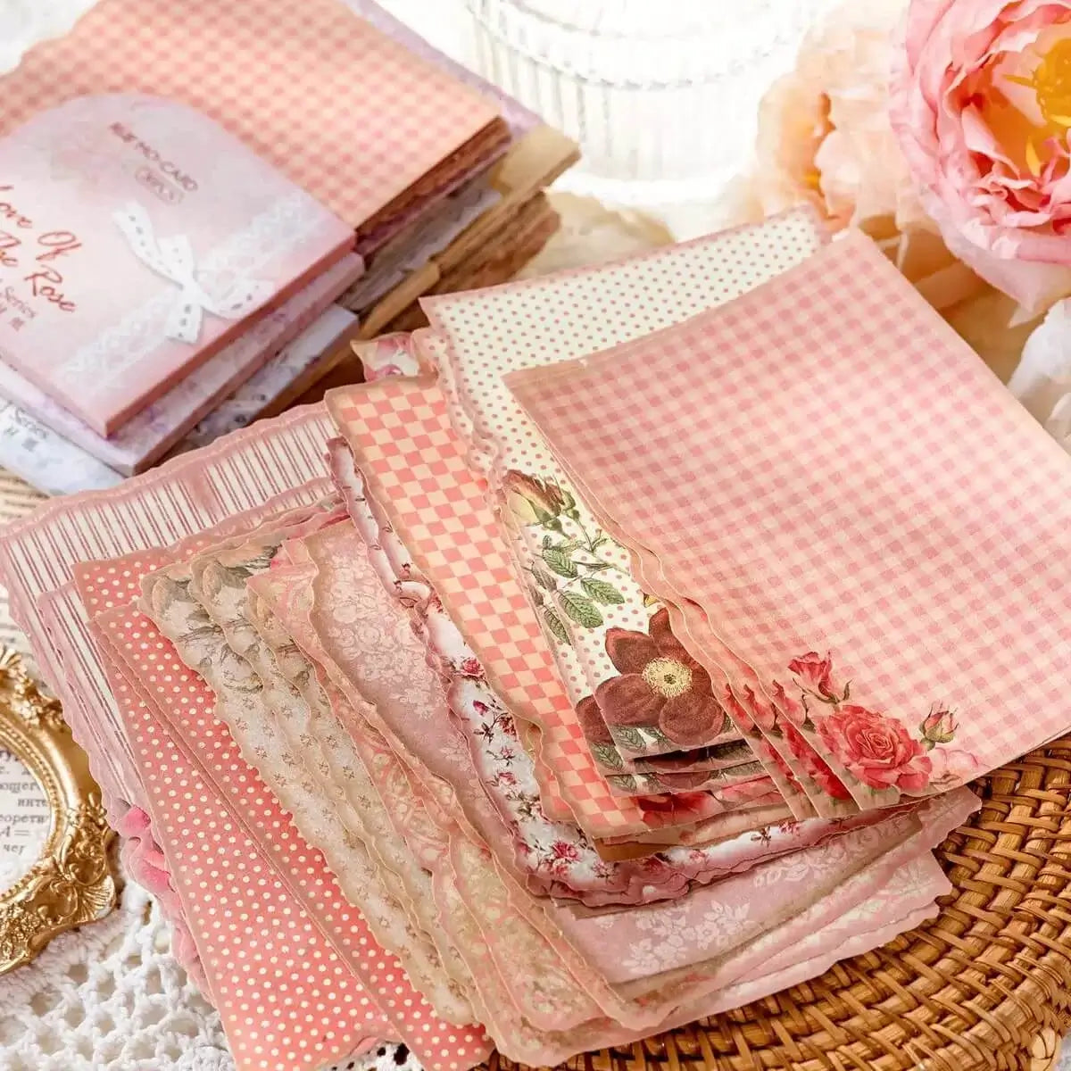 Stack of pink patterned fabric squares on a textured surface with flowers and a decorative frame.