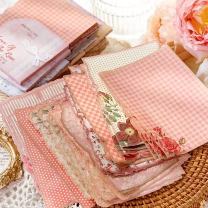 Stack of pink patterned fabric squares on a textured surface with flowers and a decorative frame.