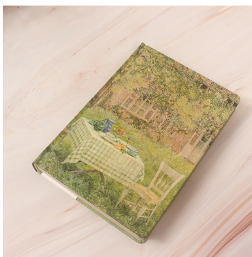 Decorative notebook with a garden scene cover on a light wooden surface