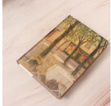 Decorative notebook with a tree and house illustration on a wooden surface