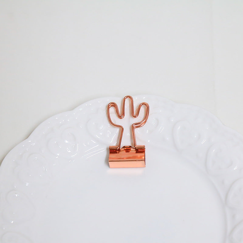 Rose gold cactus-shaped paper clip on a textured white surface