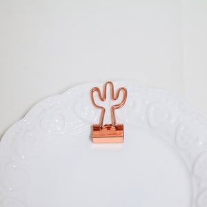 Rose gold cactus-shaped paper clip on a textured white surface