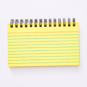 A collection of colorful coil-lined flash cards and a notepad with a wrist strap, laying on a wicker surface.