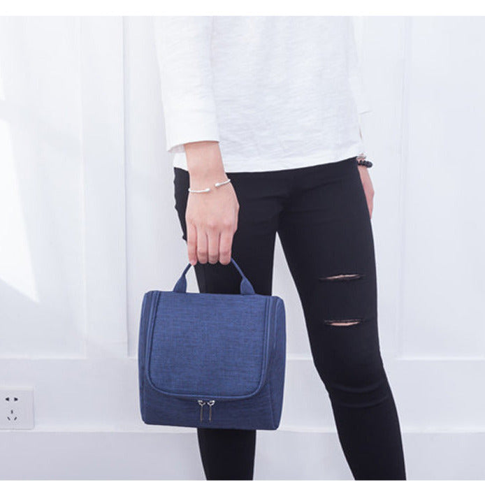 Blue handbag held by a person wearing a white shirt and black pants on a light gray background.