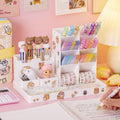 A white multifunctional desktop storage pen and stationery organizer with various holders and a sticker sheet, placed on a desk with stationery items like pens and sticky notes, and a notepad.