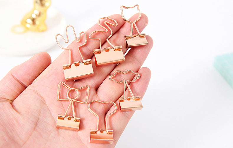 Rose gold paper clips shaped like cats held in a hand against a light background