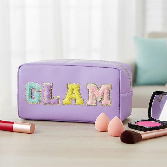 Makeup bag with 'GLAM' letters, makeup items on a table, and a blurred background.