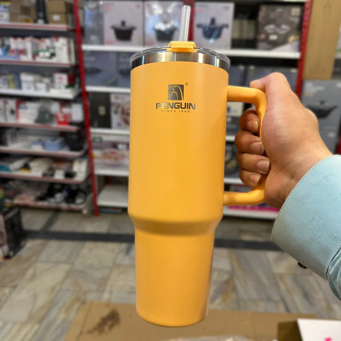 Hand holding a yellow tumbler with a straw, branded 'Penguin', in a store setting.