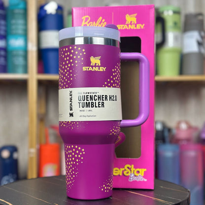 Purple Stanley tumbler with pink handle on a black surface, with a pink Stanley box in the background.