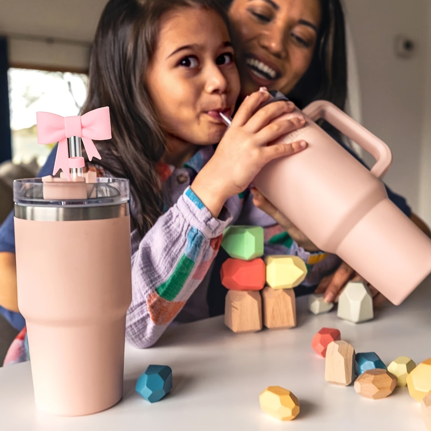 Woman and child playing with pink tumblers and building blocks on a table.