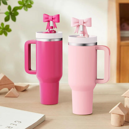 Two pink travel mugs with bow accents on a wooden surface.