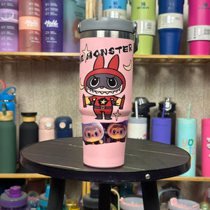 Pink tumbler with cartoon character design on a black surface with shelves of colorful tumblers in the background.