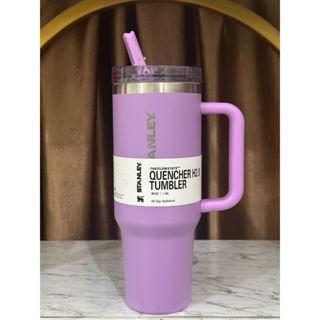 Purple tumbler with handle and straw on a wooden surface with a brown curtain background
