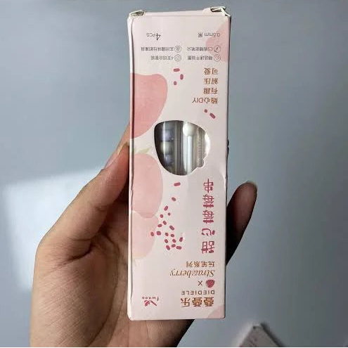 Hand holding a pink and white product box with a silver item inside, against a light background.