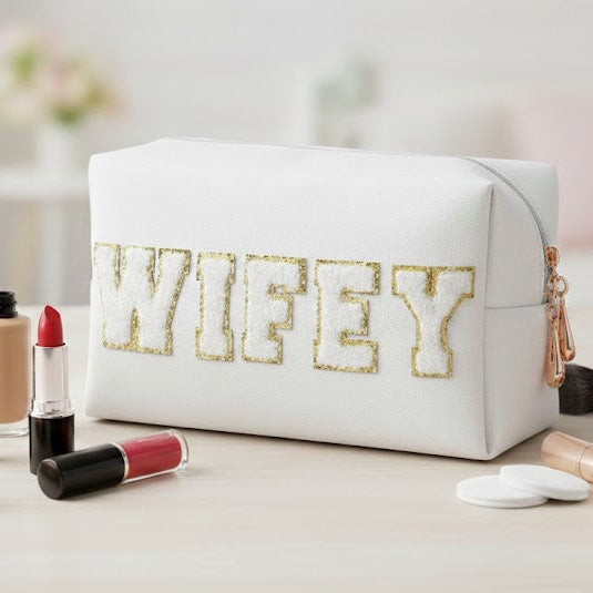 Makeup bag with 'WIFEY' text surrounded by makeup items on a light surface.