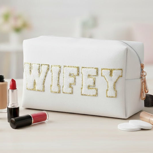 Makeup bag with 'WIFEY' text surrounded by makeup items on a light surface.