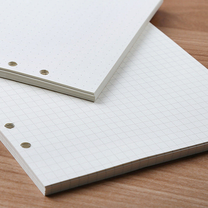 Stack of white dotted, grid, and blank pages with holes on the side for a bullet journal.