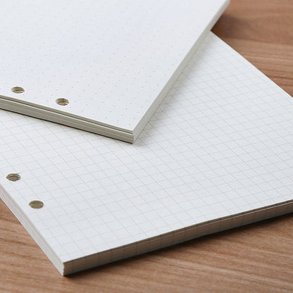 Stack of white dotted, grid, and blank pages with holes on the side for a bullet journal.